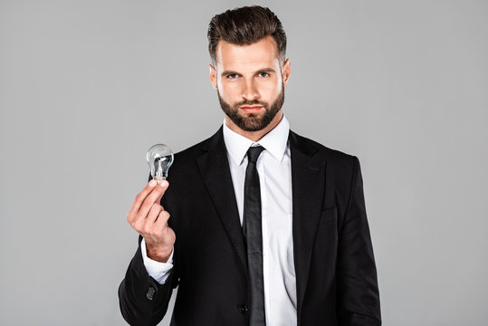 successful businessman in black suit holding light bulb isolated on grey