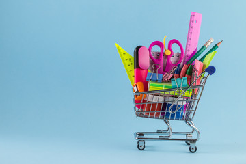 Shopping cart with different stationery on the blue background.