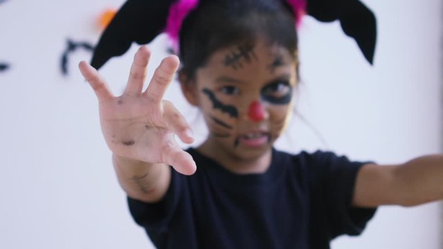 Close-up of asian little girl's hand while wagged her fingers to create a trick in halloween. The children with a painted face is posing facial expression, celebrating halloween. Slow motion.
