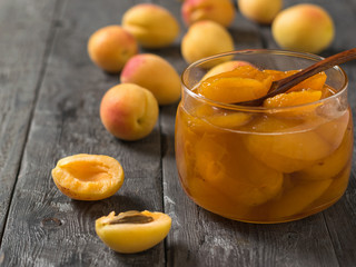 Naklejka na ściany i meble Jam of ripe apricots in a glass jar on a wooden table.