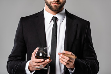 cropped view of businessman in black suit holding glass with whiskey and cigar isolated on grey