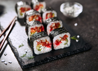 Macro photo of dragon roll with cream cheese, salmon, eel, rice, cucumber, flying fish caviar and nori. Dragon unagi maki rolls with raw red fish and tobiko on natural dark stone background close up