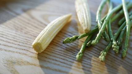 close up on baby corn and asparagus on a wooden background in light