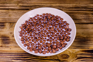 Ceramic plate with chocolate cereal balls in milk on wooden table