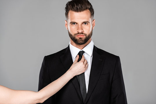 woman tying tie on businessman in black suit isolated on grey