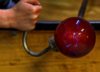 Glass blower shaping a bubble of melted glass on a rod by hand at a glass maker's workshop, shallow depth of field