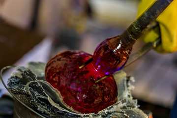 Glass blower shaping a bubble of melted glass on a rod by hand at a glass maker's workshop, shallow depth of field
