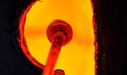 Glass blower working on a bubble of melted glass on a rod by heating it up in a kiln at a glass...