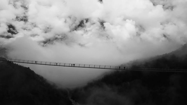 Scenic aerial profile side view of people walking on suspension bridge in black and white. suspension bridge in randa wallis switzerland.