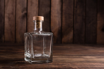 Glass transparent empty bottle with wooden plug on dark wooden background