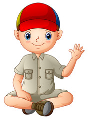 A boy in camping outfit is sitting and waving