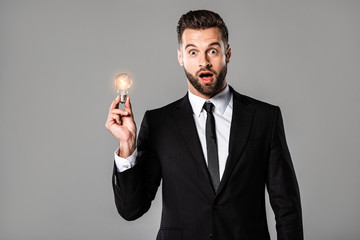 shocked businessman in black suit holding glowing light bulb isolated on grey