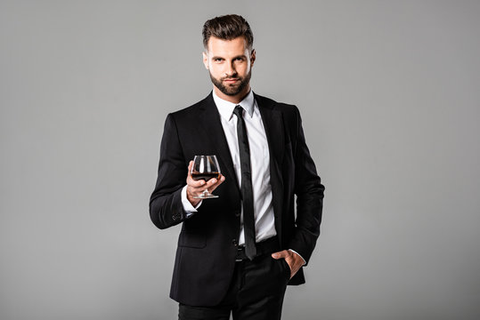 successful businessman in black suit holding glass with whiskey isolated on grey