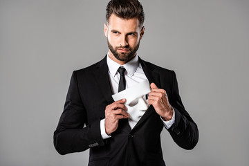 sly businessman in black suit hiding white mask isolated on grey