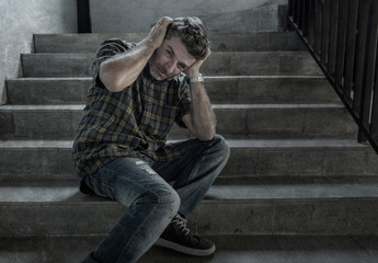 dramatic portrait of young depressed and paranoid man on dark grunge street corner staircase...