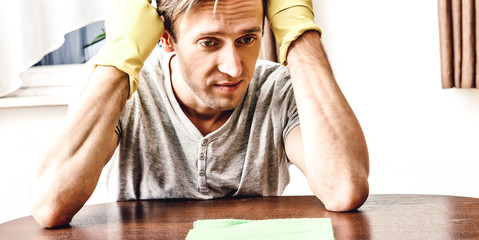 Unhappy man with gloves while cleaning table. Houseworking routine.