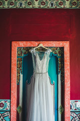 Beautiful white dress on hanger on traditional balinese textured red wooden door. Wedding concept.