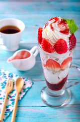 Strawberry parfait ice-cream decorated with strawberries and granola biscuits on a high glass, With a tea of ready-to-drink on a wooden floor. To feel the atmosphere in the morning.