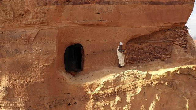 Panning drone shot of senior Orthodox priest walking on edge of steep mountain cliff at monolithic church in Tigray region, religion and culture in Ethiopia