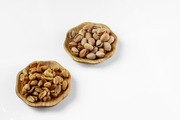 wood plates of salted peanuts and pistachios on white background. snack to beer