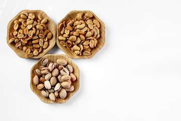 wood plates of salted peanuts and pistachios on white background. snack to beer