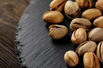 top view of salted pistachio nuts on stone board on wood background. copy space