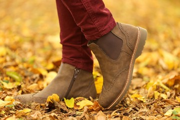 Autumn time. Autumn shoes . Female legs in brown boots on yellow maple leaves. 