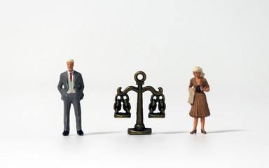 A miniature man and a miniature woman standing on both sides of the scale.