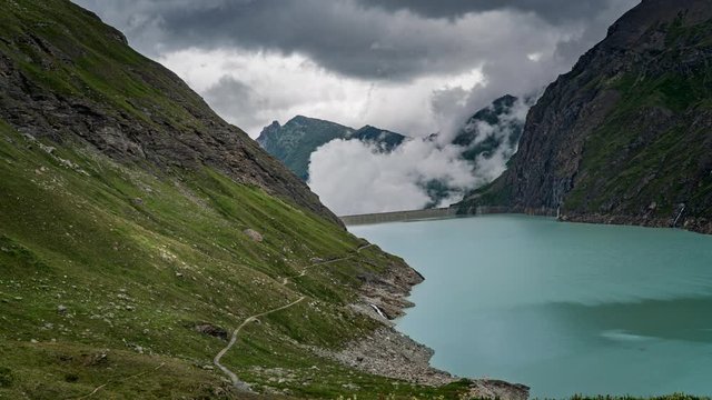 Timelapse of a swiss reservoir in the alps. Fast moving clouds are rising above the dam and the mountains. 4k 4096x2304