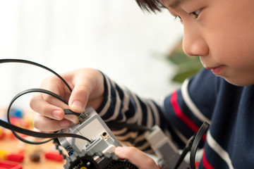 Closeup: Smart looking preteen / teenage Asian boy assembles blocks Mindstorms EV3 for school project with focus and concentration. STEM Education, Programming, Robotics Technology, Online Learning.