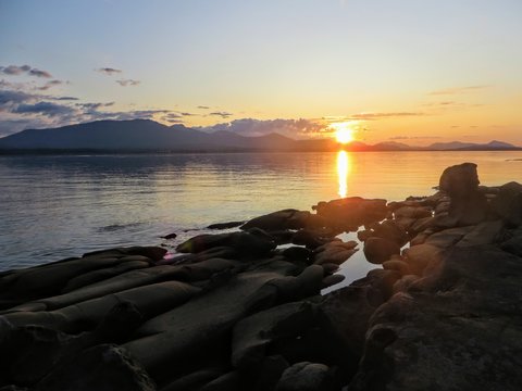 A rocky shoreline overlooking the ocean during sundown.  The sun is reflecting and glowing off of the water and tidal pools within the rocks.  It is a serene and peaceful setting.