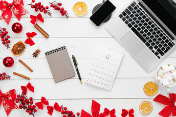 Laptop on white wooden desk surrounded with red Christmas decorations, top view