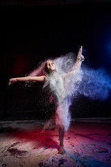 Small jumping girl during photoshoot with flour in dark studio