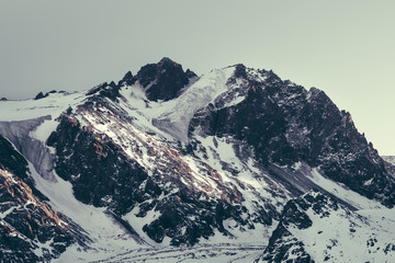 Aerial view of misty mountains, lake and clouds above the mountain peaks, opposite the sunlight, blue tinted.