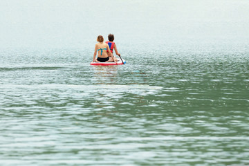 Two young girls are floating on a Board La sup surfing on the lake.