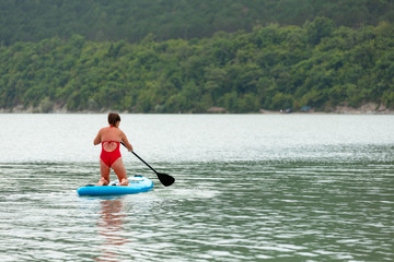 Fototapeta na wymiar Young girl floating on a Board La sup surfing on the lake.