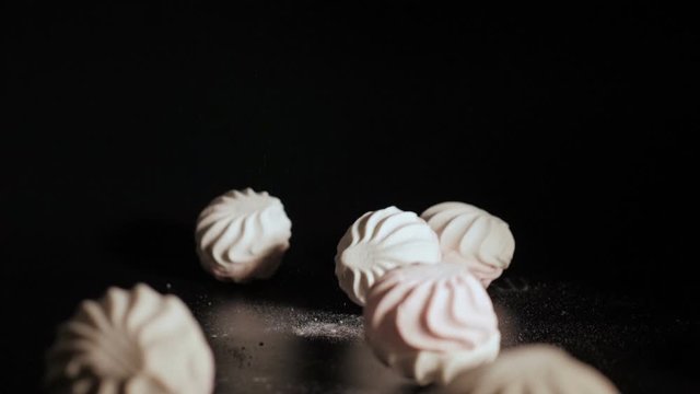 Zefir falling close up. White pieces of marshmallow fall in slow motion a black background and bounce off each other. Closeup.