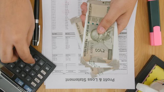 A company accountant reading profit and loss account and and counting cash in hand. 