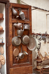 View of front of the flea shop with vintage and ancient kitchen utencils, pots and lamps hanged on brown wooden door.