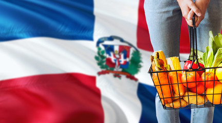 Woman is holding supermarket basket, Dominican Republic waving flag background. Economy concept for...