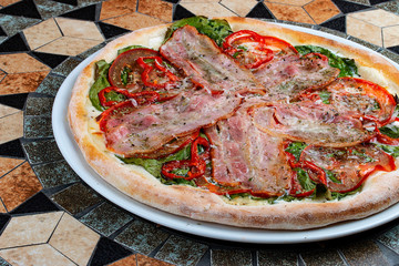 Pizza with bacon, tomatoes, pepper and spinach on the stone table