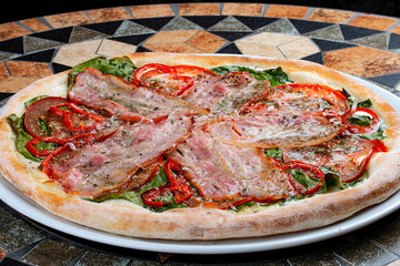 Pizza with bacon, tomatoes, pepper and spinach on the stone table