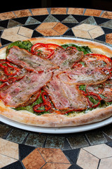 Pizza with bacon, tomatoes, pepper and spinach on the stone table