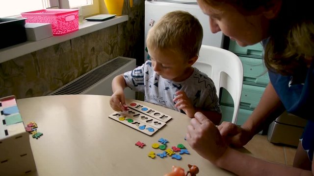 autistic child collects colored jigsaw puzzles in forms with the help of a teacher