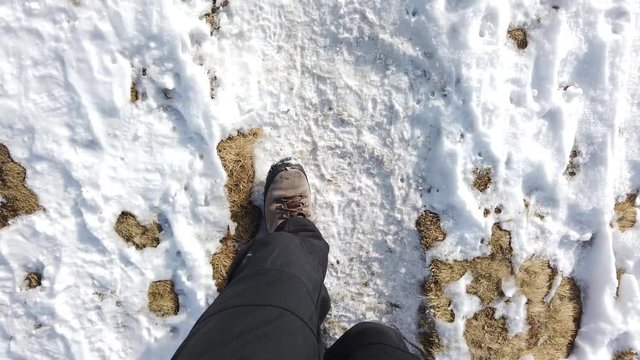 Hiker point of view. POV closeup of a people walking on the mountain path between grass and snow