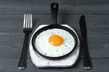 fried eggs in cast iron pan on white wooden stand with cutlery