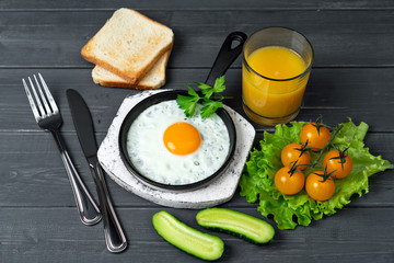 fried eggs in cast iron pan on white wooden stand with yellow cherry tomatoes, orange juice, toasts...