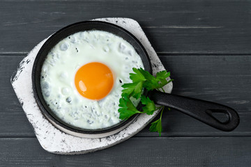 fried eggs in cast iron pan on white wooden stand with parsley