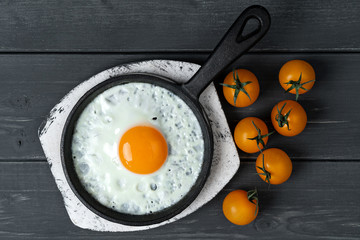 fried eggs in cast iron pan on white wooden stand with yellow cherry tomatoes. Easy healthy breakfast.