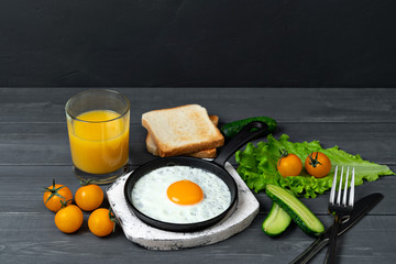 fried eggs in cast iron pan on white wooden stand with yellow cherry tomatoes, orange juice, toasts...